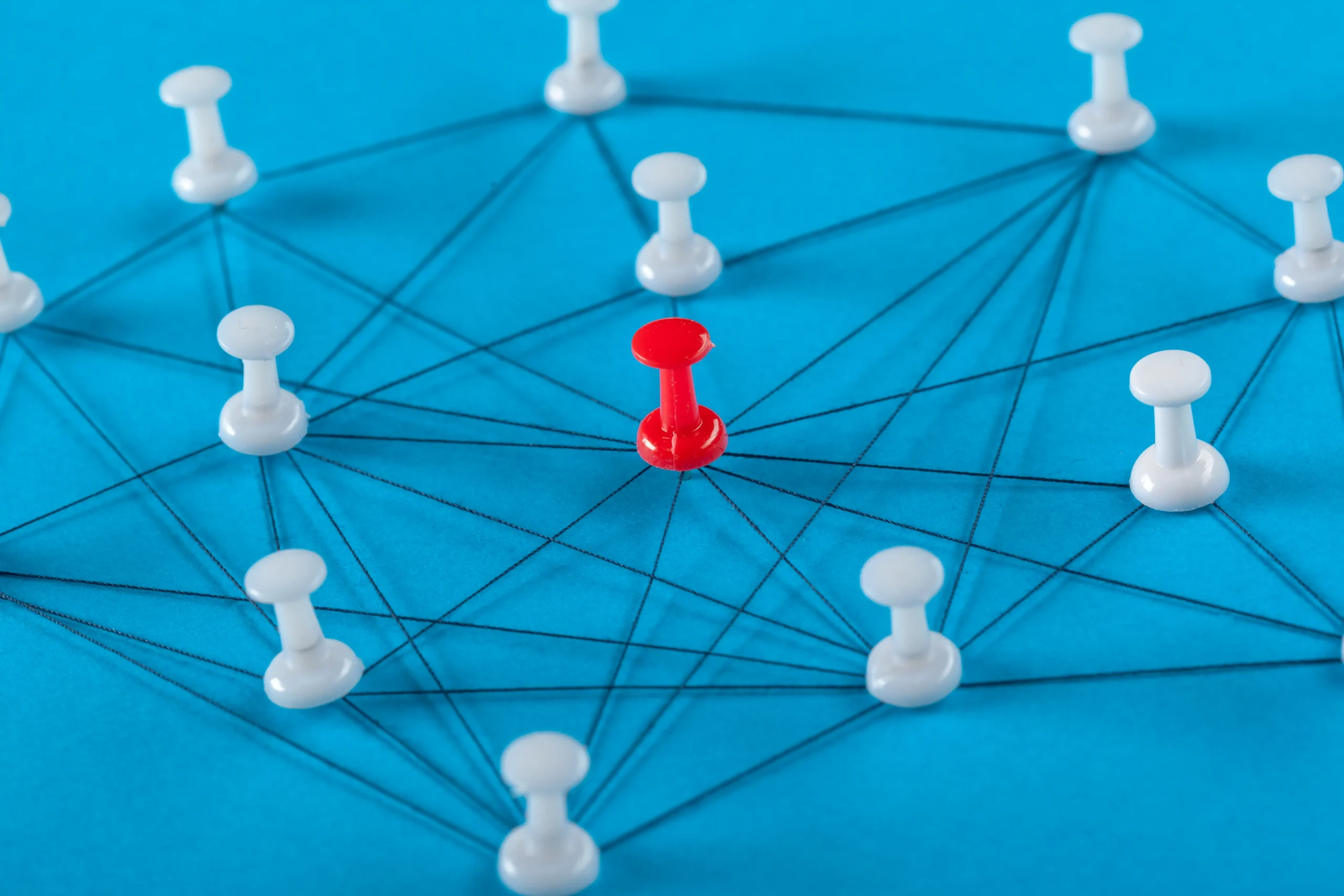 A red pushpin at the center connected by black strings to several surrounding white pushpins on a blue background