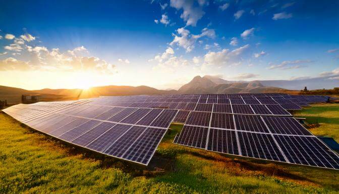 Solar panels in a field during sunrise with mountains in the background.