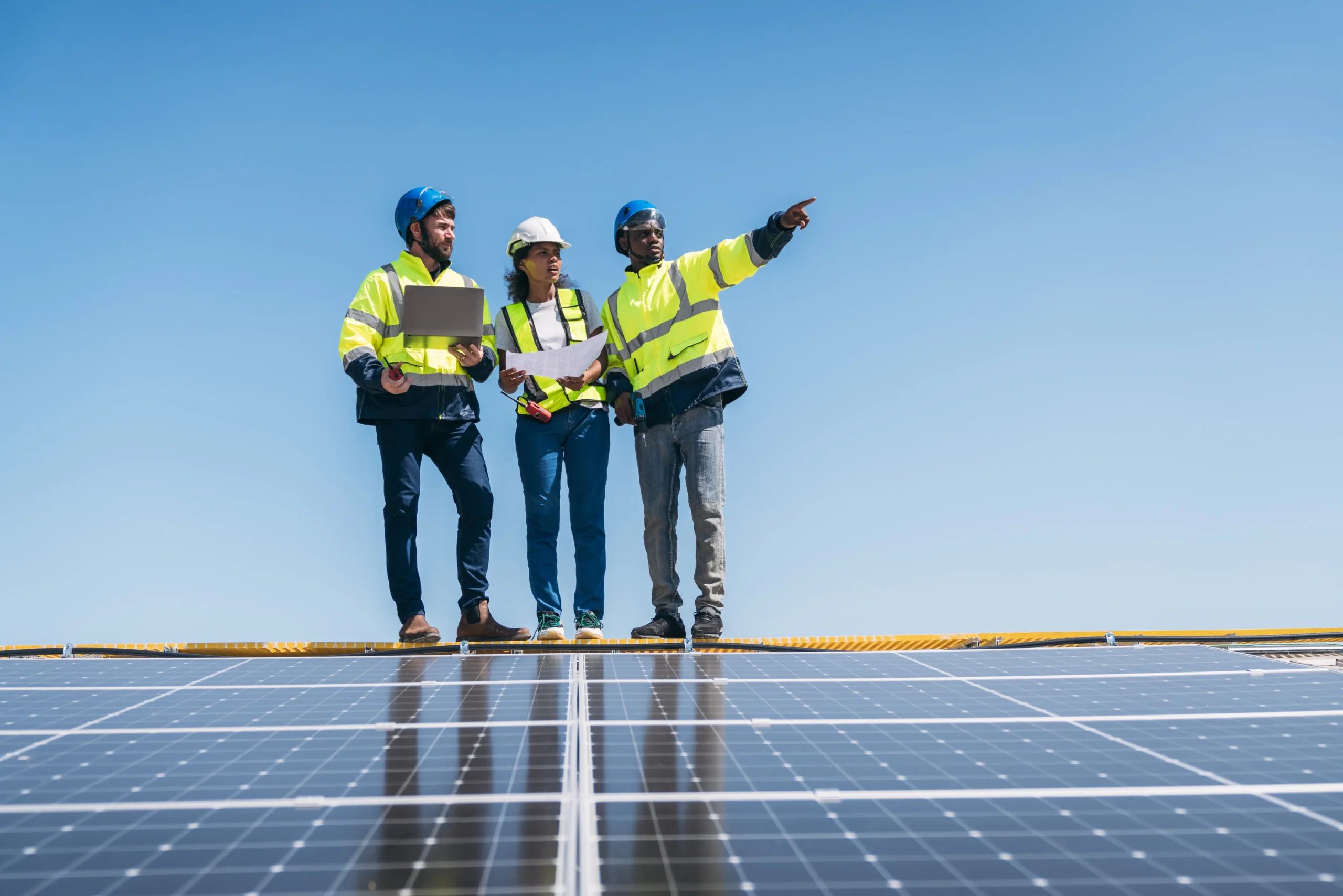 Three engineers in safety gear inspecting solar panels