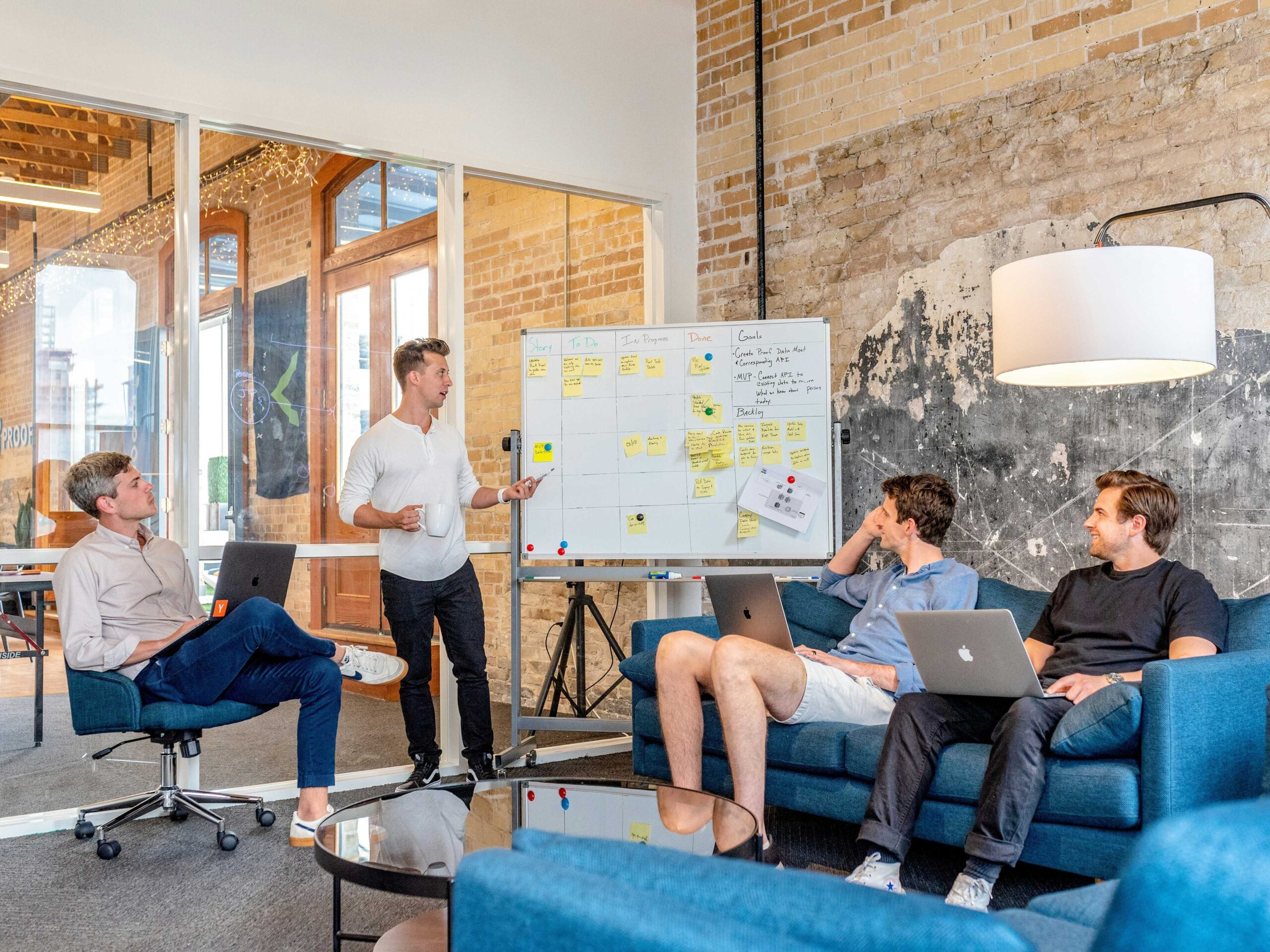 A group of people is gathered in a room, actively engaged with their laptops and collaborating around a whiteboard